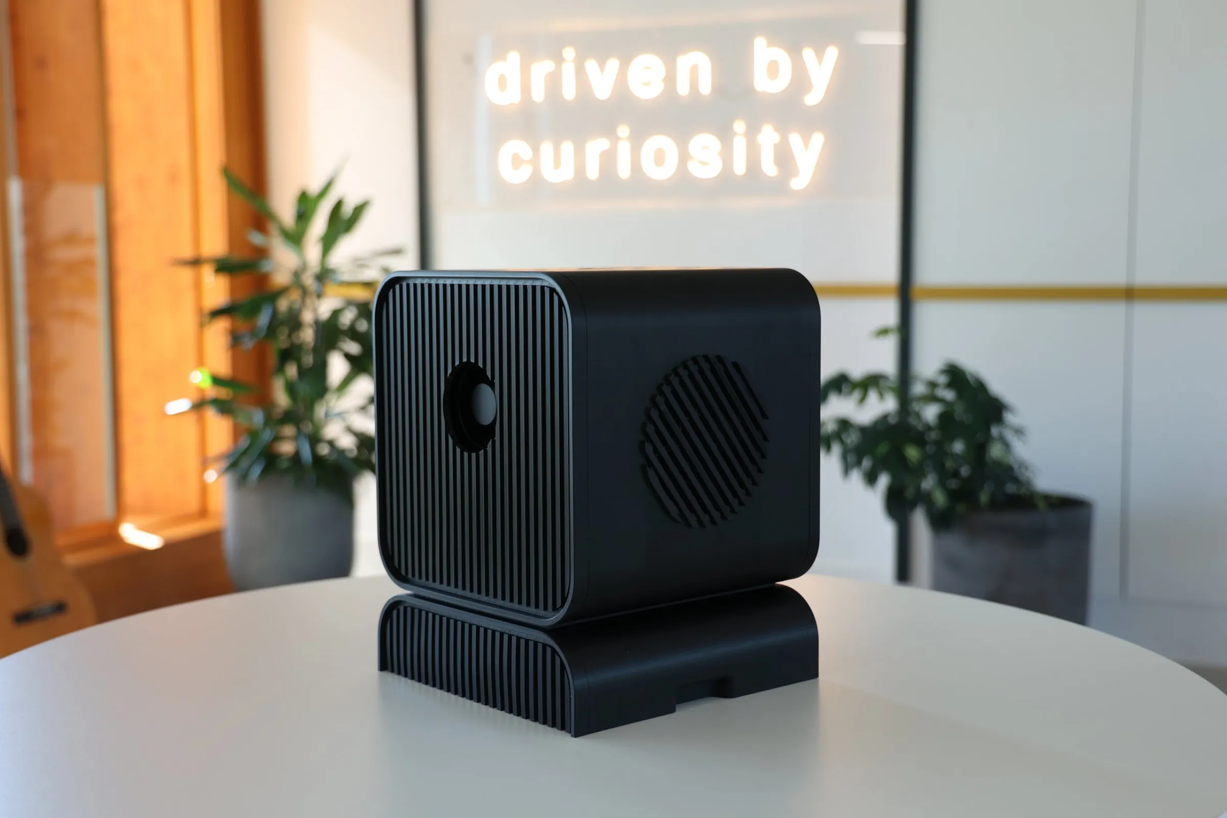 The Local AI Workstation on a table in the Empathy office, in front of a neon sign that reads driven by curiosity.